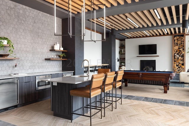 kitchen featuring decorative backsplash, sink, light parquet flooring, fridge, and a breakfast bar area