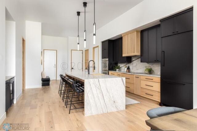 kitchen featuring pendant lighting, light brown cabinets, a kitchen island with sink, built in fridge, and decorative backsplash