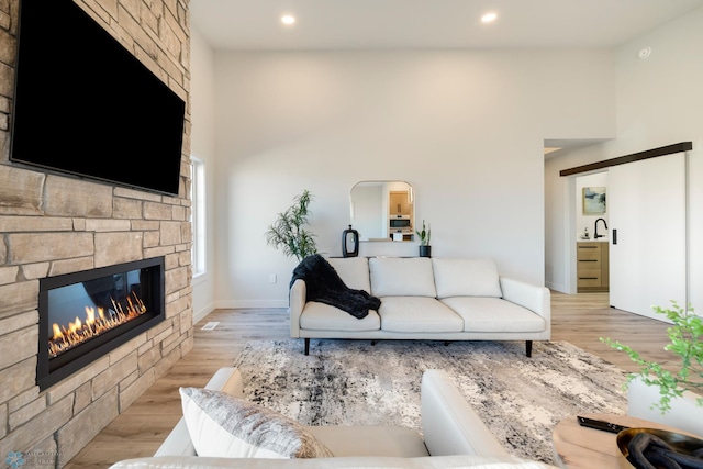 living room featuring a towering ceiling, light hardwood / wood-style floors, a stone fireplace, and sink