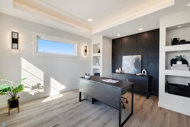 office space featuring a raised ceiling, built in features, wooden walls, and light hardwood / wood-style flooring