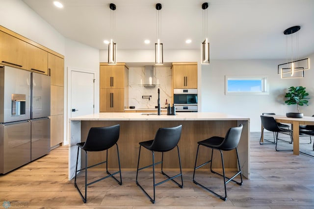 kitchen with light brown cabinets, hanging light fixtures, stainless steel appliances, light hardwood / wood-style floors, and a spacious island