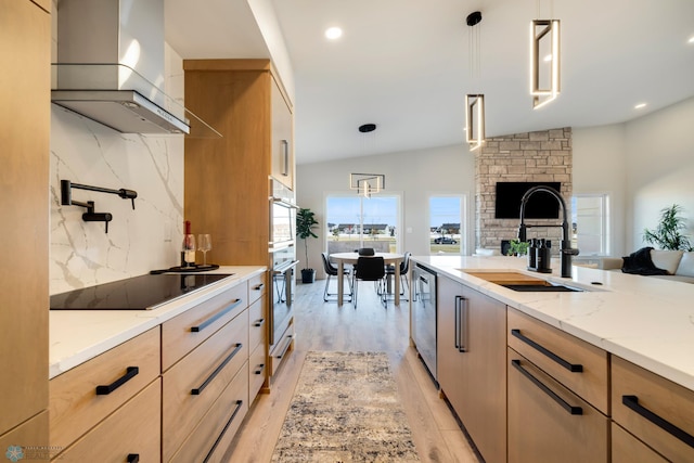 kitchen featuring sink, stainless steel appliances, hanging light fixtures, wall chimney range hood, and light hardwood / wood-style flooring