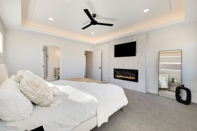 carpeted bedroom with ceiling fan, ensuite bath, multiple windows, and a tray ceiling