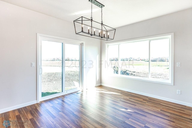 unfurnished dining area with dark hardwood / wood-style floors, a healthy amount of sunlight, and a notable chandelier