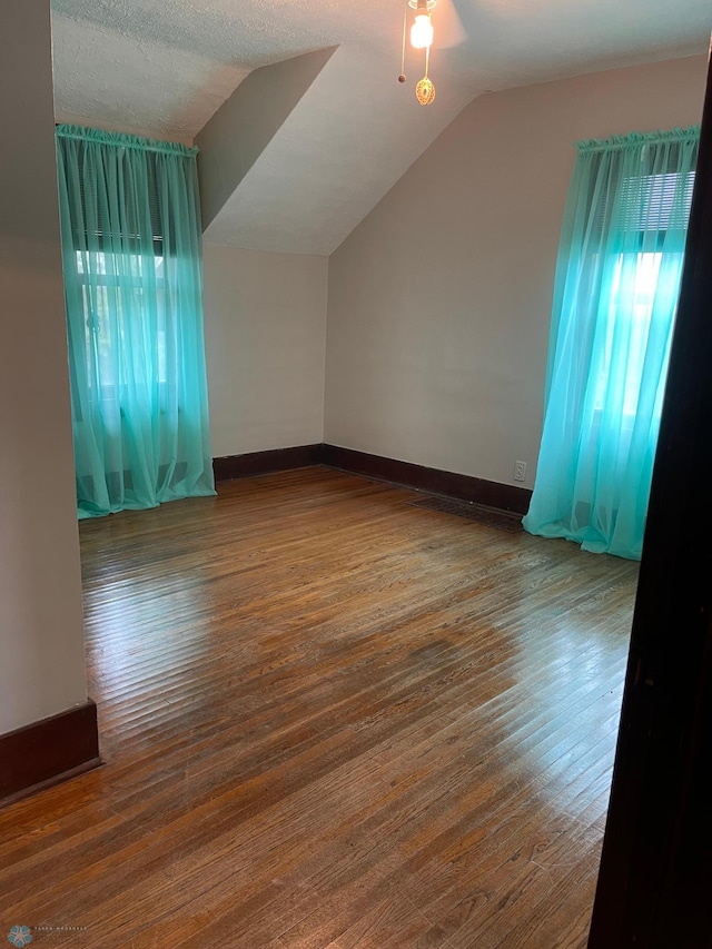 bonus room featuring ceiling fan, vaulted ceiling, a textured ceiling, and dark wood-type flooring