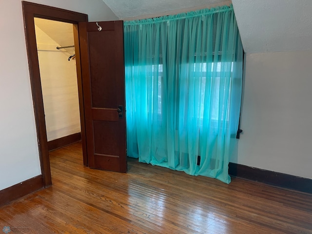 unfurnished bedroom featuring a textured ceiling, vaulted ceiling, and hardwood / wood-style floors