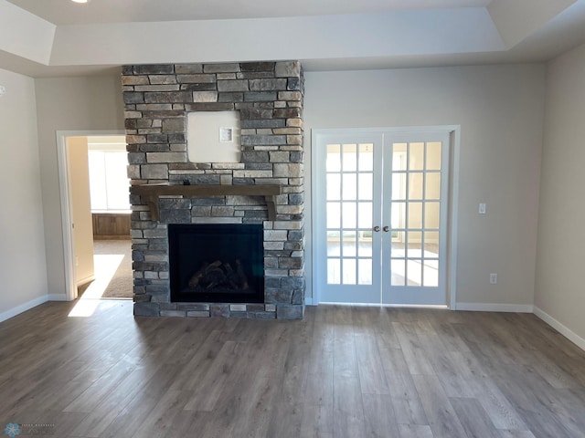 unfurnished living room featuring hardwood / wood-style floors, a stone fireplace, a tray ceiling, and french doors