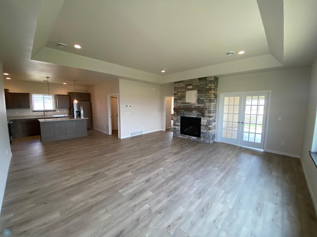 unfurnished living room with a tray ceiling, baseboards, recessed lighting, and light wood finished floors