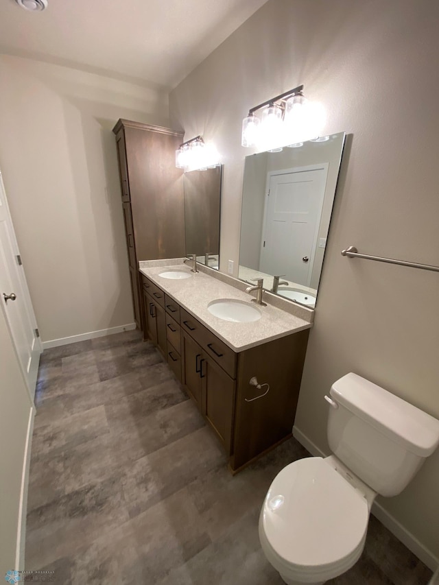 bathroom with toilet, double vanity, and baseboards