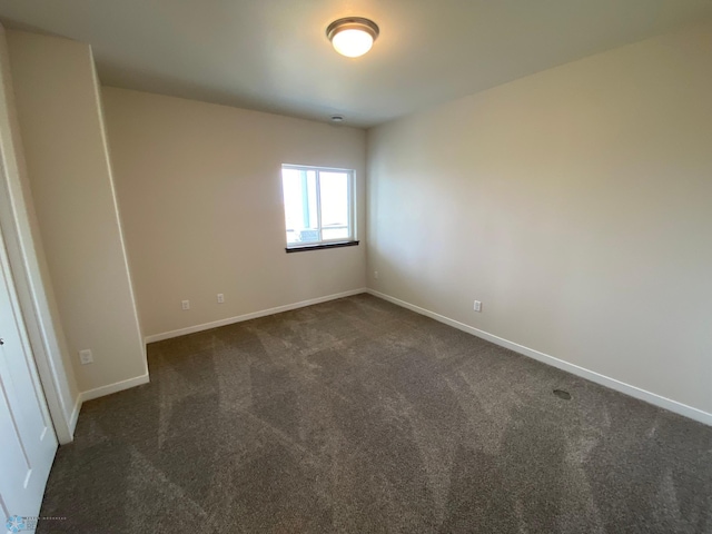 spare room featuring dark carpet and baseboards