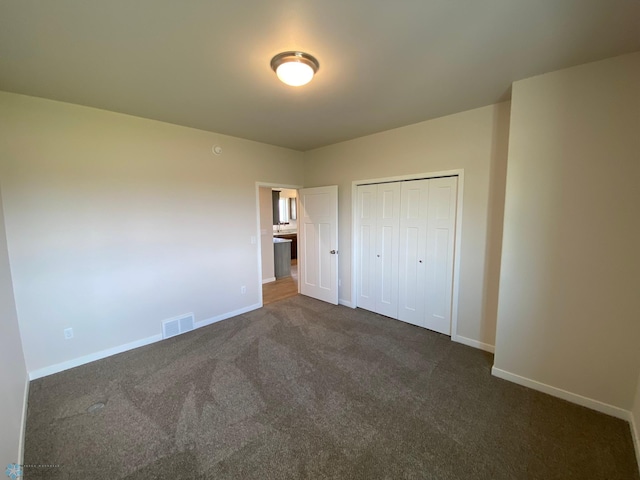 unfurnished bedroom with dark carpet, baseboards, and a closet