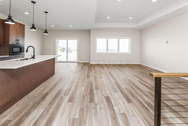 kitchen with light hardwood / wood-style floors, sink, stainless steel microwave, and hanging light fixtures