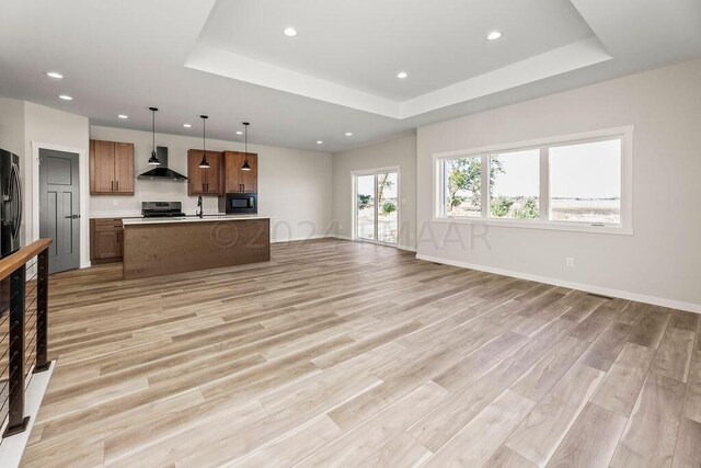 kitchen with a raised ceiling, decorative light fixtures, light wood-type flooring, and wall chimney range hood