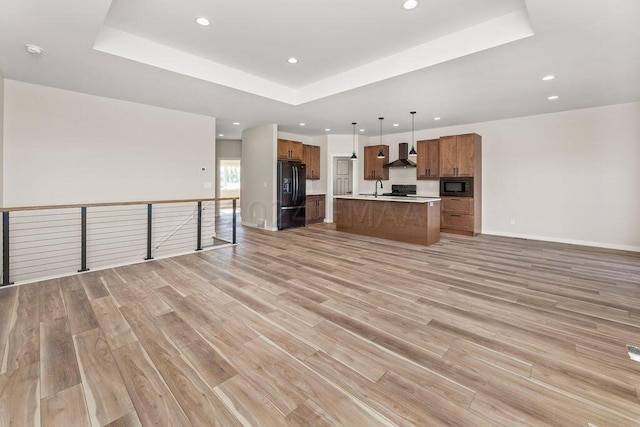 unfurnished living room with sink, light wood-type flooring, and a raised ceiling