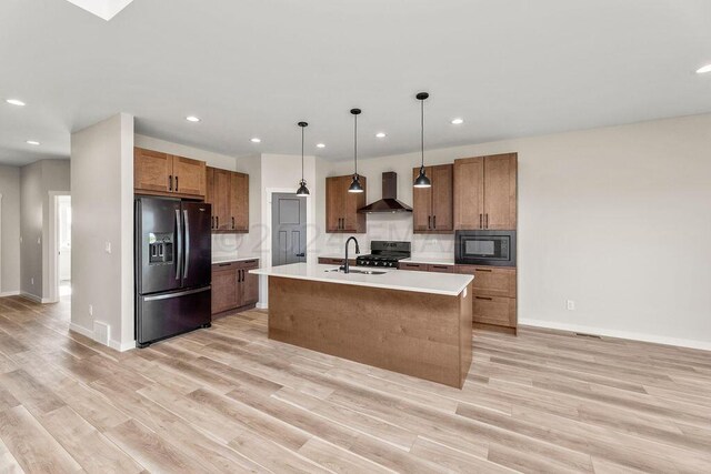 kitchen with black appliances, light hardwood / wood-style flooring, a kitchen island with sink, and wall chimney range hood