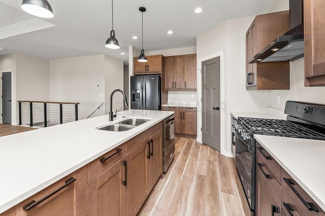 kitchen with light hardwood / wood-style flooring, black appliances, hanging light fixtures, wall chimney exhaust hood, and sink