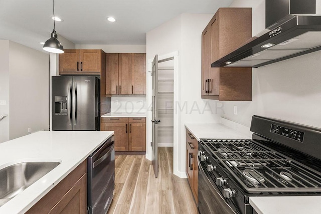 kitchen featuring gas range, decorative light fixtures, stainless steel refrigerator with ice dispenser, light wood-type flooring, and wall chimney exhaust hood