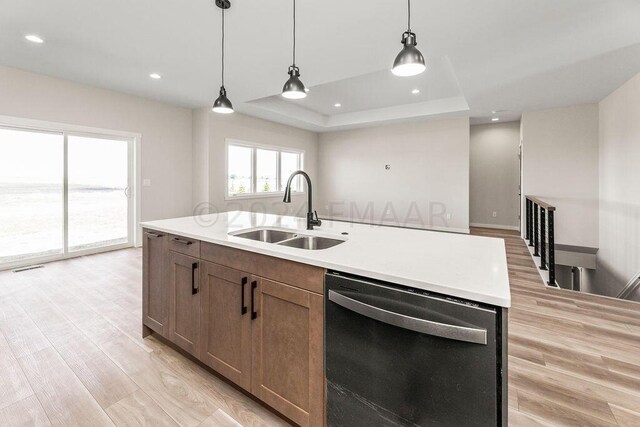 kitchen featuring sink, dishwashing machine, a kitchen island with sink, light wood-type flooring, and a raised ceiling