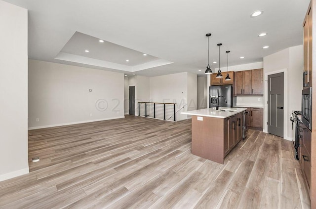 kitchen featuring a tray ceiling, light hardwood / wood-style flooring, a center island with sink, and stainless steel fridge with ice dispenser