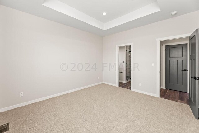 unfurnished bedroom featuring dark colored carpet and a raised ceiling