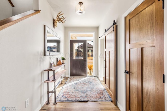 entryway featuring light wood-style flooring, baseboards, and a barn door