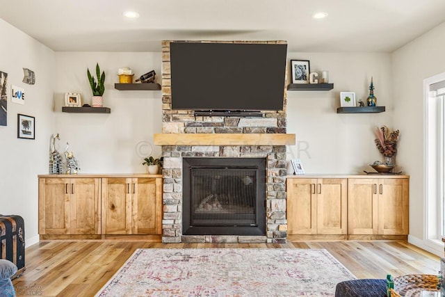 living area with recessed lighting, baseboards, a stone fireplace, and wood finished floors