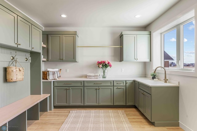 kitchen with green cabinetry, light countertops, light wood-type flooring, and a sink