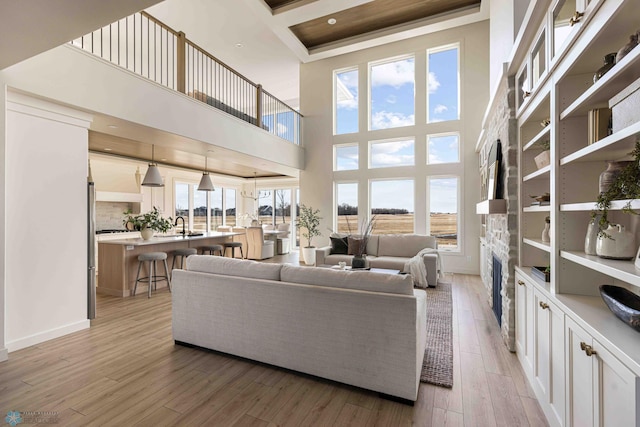 living area with baseboards, a towering ceiling, light wood-style floors, and a fireplace