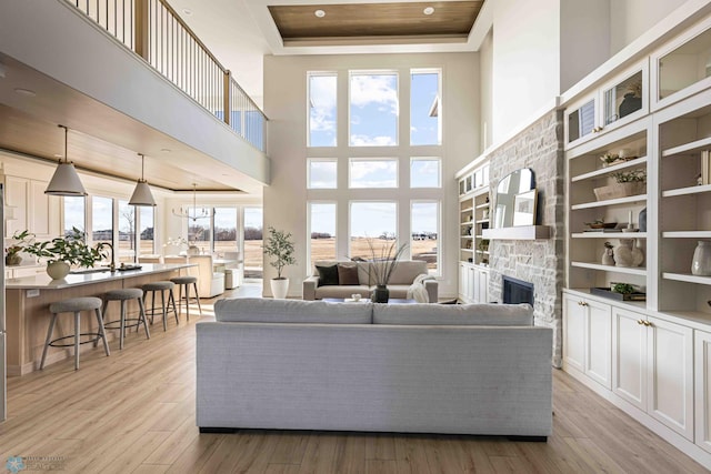 living area featuring light wood-style flooring, a high ceiling, a tray ceiling, and a stone fireplace