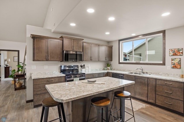 kitchen with light wood-type flooring, stainless steel appliances, a kitchen island, and sink