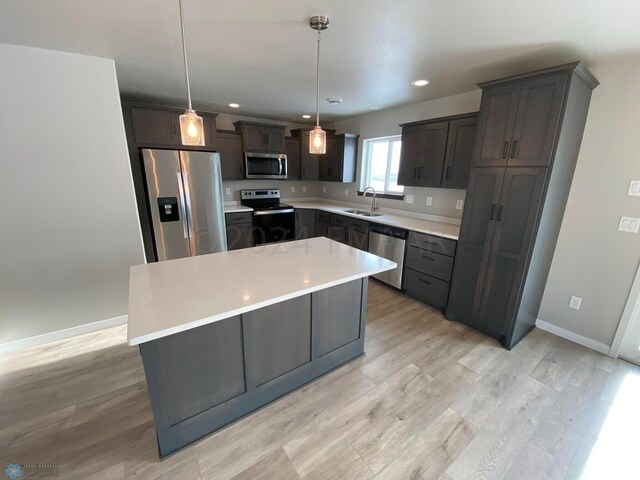 kitchen featuring appliances with stainless steel finishes, sink, decorative light fixtures, light hardwood / wood-style floors, and a kitchen island