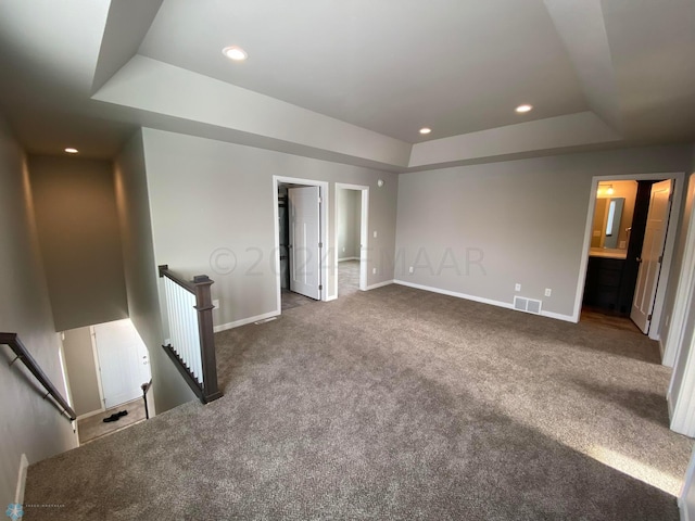 unfurnished bedroom featuring a raised ceiling, ensuite bath, and dark colored carpet