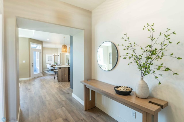 hall with light hardwood / wood-style flooring and a notable chandelier