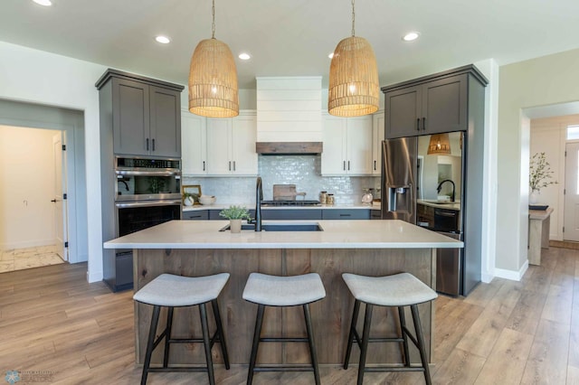 kitchen featuring appliances with stainless steel finishes, a center island with sink, light hardwood / wood-style floors, and white cabinets