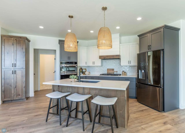 kitchen featuring appliances with stainless steel finishes, white cabinetry, an island with sink, light wood-type flooring, and sink