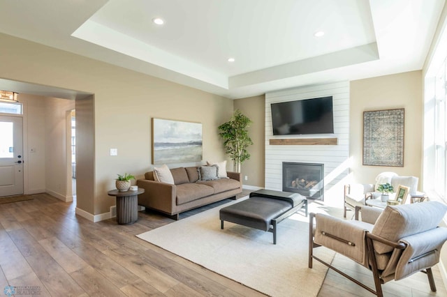 living room with light hardwood / wood-style flooring, a raised ceiling, and a fireplace