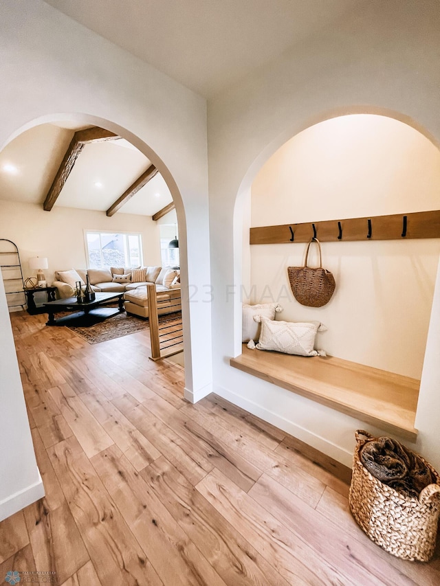 interior space featuring beamed ceiling, baseboards, arched walkways, and light wood finished floors