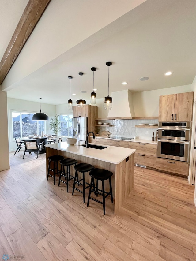 kitchen with tasteful backsplash, sink, hanging light fixtures, stainless steel appliances, and a center island with sink