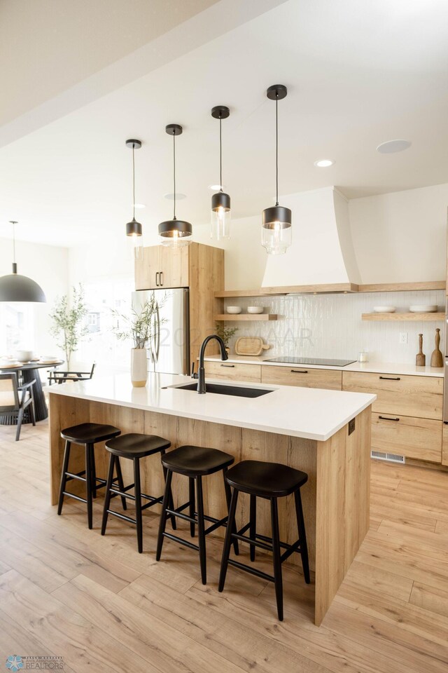 kitchen featuring stainless steel fridge, sink, hanging light fixtures, and a large island with sink