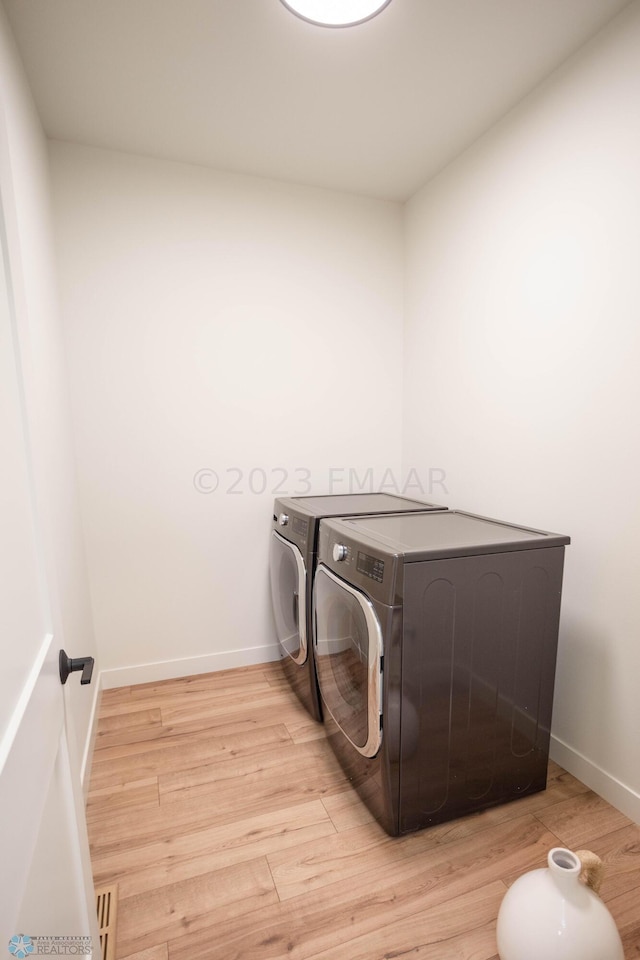 laundry room with washing machine and clothes dryer and light hardwood / wood-style flooring