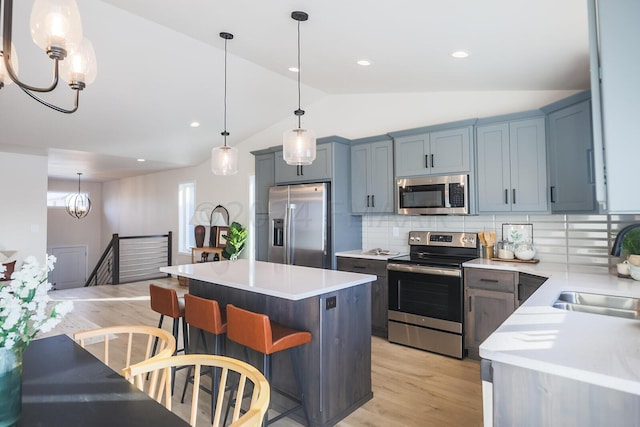 kitchen featuring a kitchen bar, hanging light fixtures, backsplash, vaulted ceiling, and stainless steel appliances