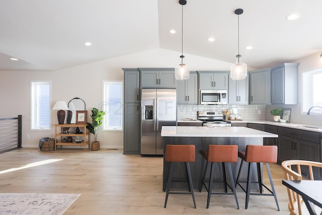 kitchen featuring appliances with stainless steel finishes, light hardwood / wood-style flooring, lofted ceiling, pendant lighting, and a center island