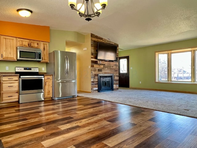 kitchen featuring a notable chandelier, stainless steel appliances, a fireplace, open floor plan, and vaulted ceiling