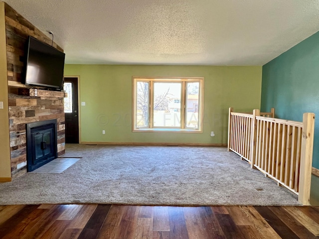 unfurnished living room featuring a textured ceiling, a fireplace, wood finished floors, and baseboards