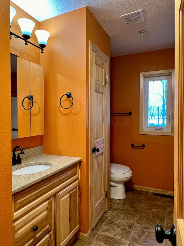 bathroom featuring visible vents, toilet, a textured ceiling, vanity, and baseboards