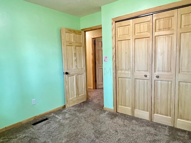 unfurnished bedroom featuring a closet, visible vents, dark carpet, and baseboards