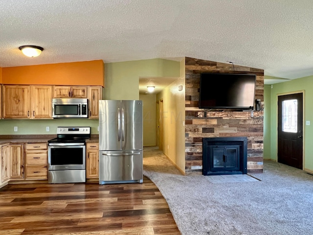 kitchen featuring lofted ceiling, a large fireplace, stainless steel appliances, dark countertops, and dark wood finished floors