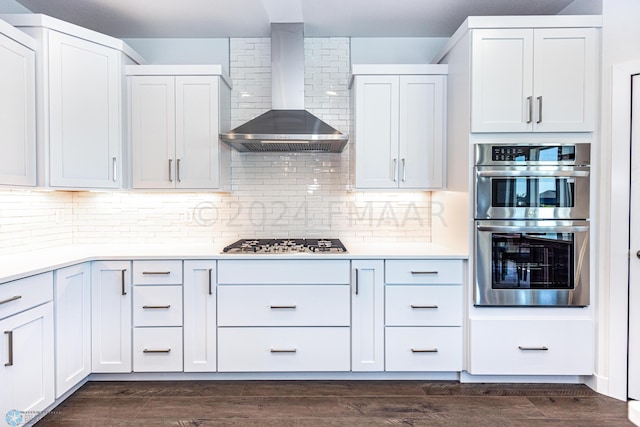 kitchen with wall chimney range hood, dark hardwood / wood-style flooring, appliances with stainless steel finishes, white cabinets, and backsplash