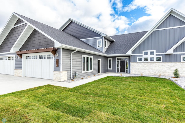 view of front facade with an attached garage, a shingled roof, driveway, stone siding, and a front lawn