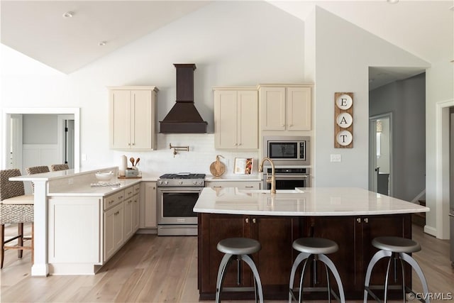 kitchen with appliances with stainless steel finishes, a breakfast bar area, light wood-type flooring, premium range hood, and sink